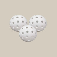 Three white Recess Pickleball hybrid outdoor pickleballs grouped together on tan background